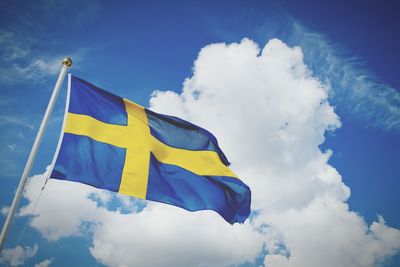 Low angle view of swedish flag against cloudy sky