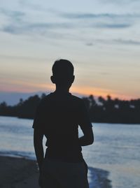 Silhouette man looking at sea against sky during sunset