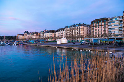 River by buildings in city against sky at dusk