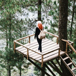 Rear view of woman standing on footbridge in forest