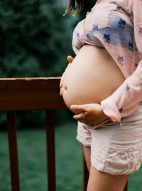 Midsection of pregnant woman touching belly while standing outdoors