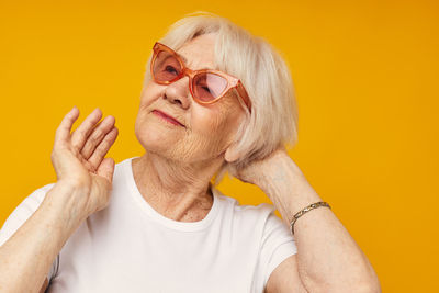 Portrait of young woman wearing sunglasses against yellow background