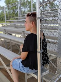 Young woman sitting on bleachers by chainlink fence