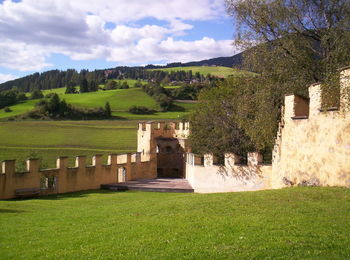 Fortified wall amidst grassy field against cloudy sky