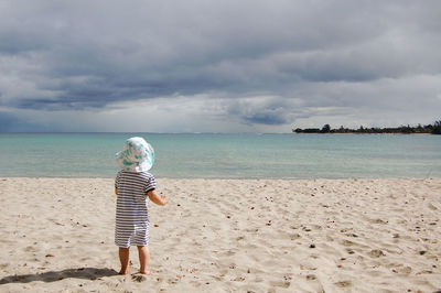 Rear view of toddler girl on beach against sky
