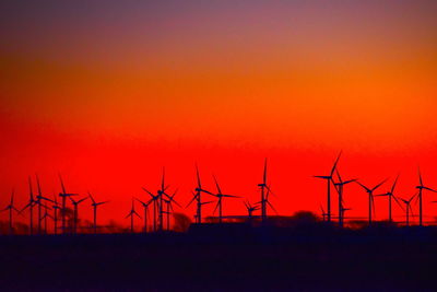 Silhouette of wind turbines on field against orange sky