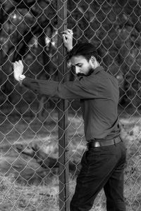 Young man standing by chainlink fence in cage