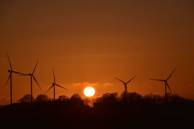 Silhouette wind turbines on field against sky during sunset