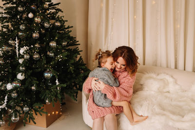 Portrait of smiling young woman standing by christmas tree at home