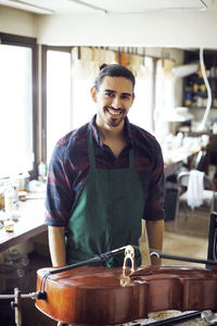 Portrait of smiling man standing by violin in workshop