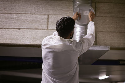 Rear view of man checking air duct