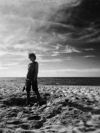 Rear view of woman standing at beach against sky