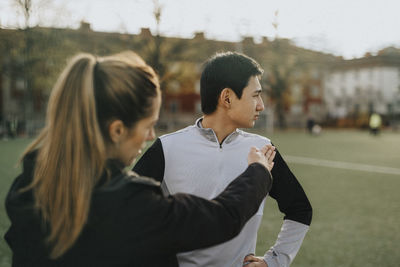 Female coach talking with male athlete while standing in sports field