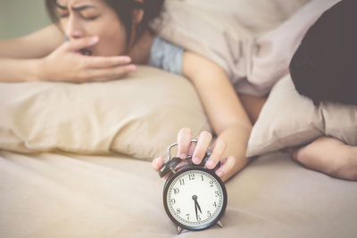 Close-up of woman holding alarm clock while sleeping in bed