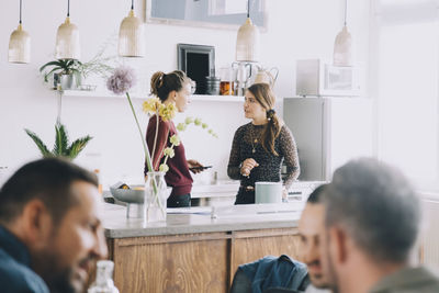 Creative female entrepreneurs discussing at kitchen island while colleagues in foreground at office