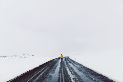 Mid distance of man standing on road amidst snow field against sky