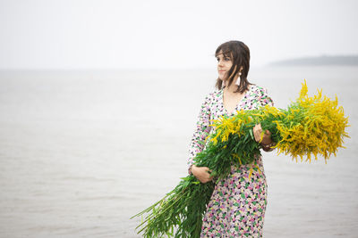 Young beautiful woman with a large bouquet of wild flowers posing on the beach