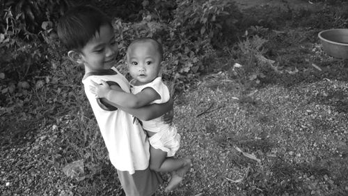 High angle view of boy carrying baby on field