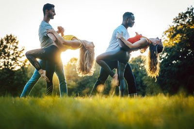 Surface level image of couple dancing on grassy field against clear sky during sunset