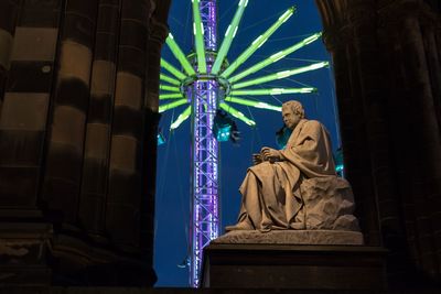 Low angle view of statue against illuminated chain swing ride