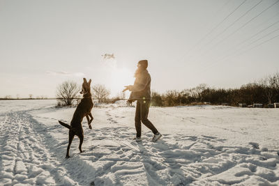 Teenage girl playing with dog in snow at winter sunrise