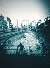 Shadow of man on railroad track in city against clear sky