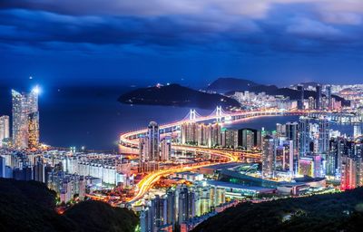 Illuminated city by sea against sky at night