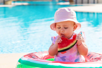 Cute girl eating watermelon sitting on tube in pool
