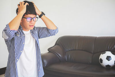 Sad young man with hands in hair watching tv at home