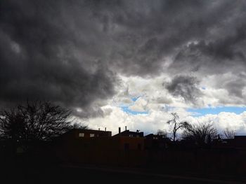 Silhouette of bare trees against cloudy sky