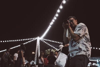 Low angle view of man photographing while standing against sky at night