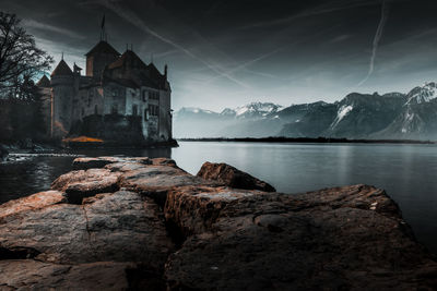 Rock by lake and buildings against sky