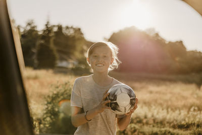 Portrait of smiling boy holding soccer ball at sunny day