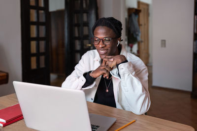 Cheerful inspired african american man smiling looking at laptop screen sits at table in apartment