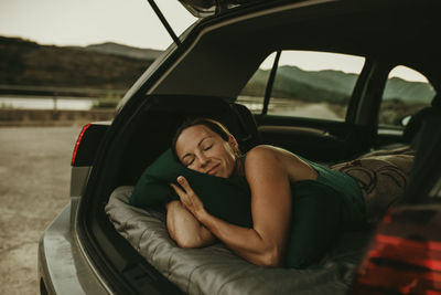 Tired woman sleeping in cozy car trunk at dusk