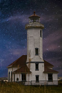 Low angle view of lighthouse by building against sky at night