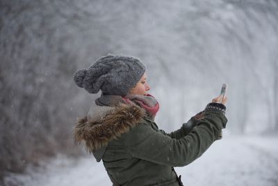 Side view of woman photographing through smart phone during winter