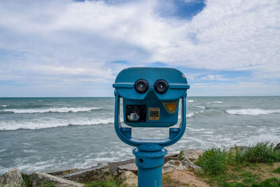 Coin-operated binoculars by sea against sky