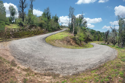 Empty road by trees against sky