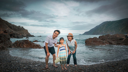 Portrait of parents with daughter standing at beach against sky