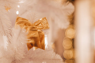 Golden christmas bow hanging on the white christmas tree. magic details with bokeh lights