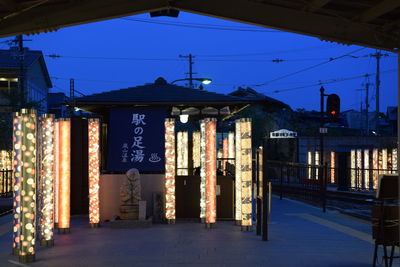 Illuminated lanterns hanging by building against sky at dusk