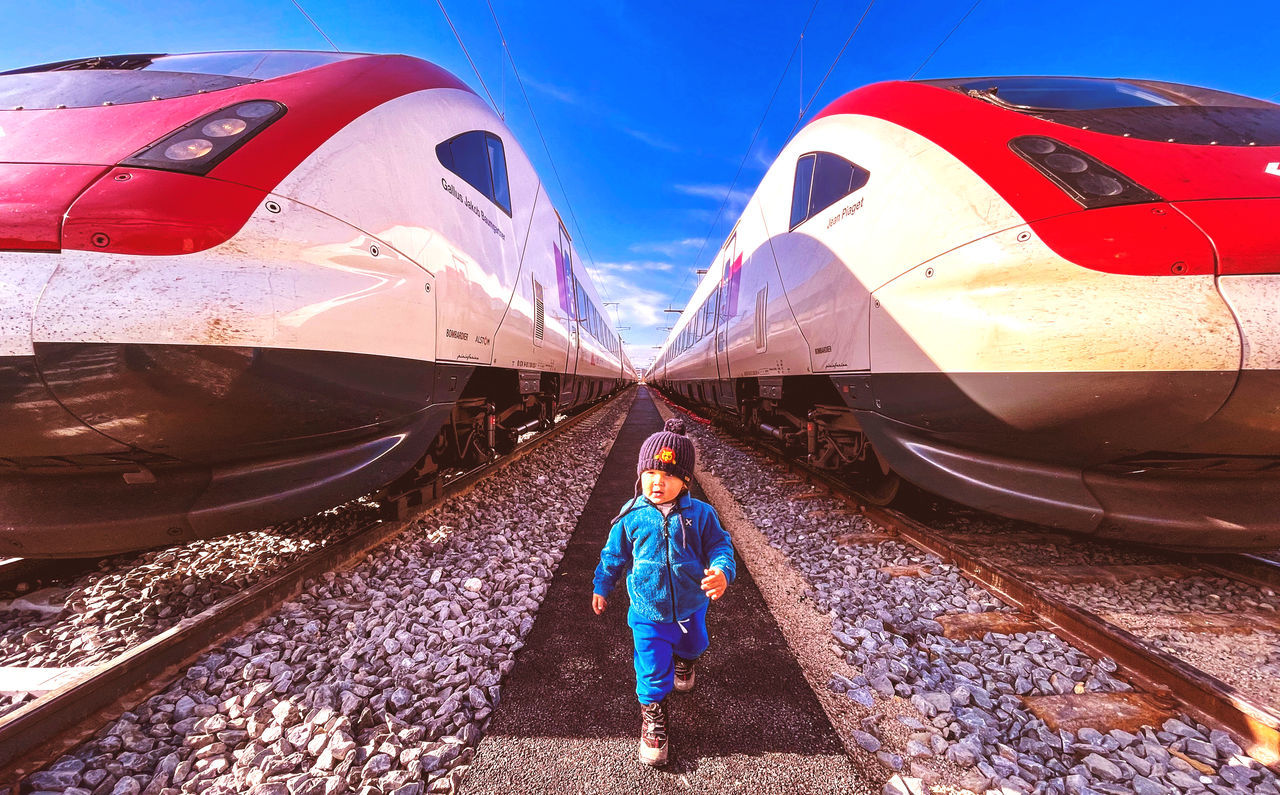 transportation, one person, mode of transportation, air vehicle, aircraft, travel, vehicle, full length, sky, standing, adult, nature, airplane, aviation, blue, transport, high-speed rail, train, front view, adventure, outdoors, day, airliner, sunlight, women, bullet train, young adult, clothing, portrait, childhood, red, person