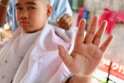 Portrait of boy showing stop gesture with barber cutting hair in background