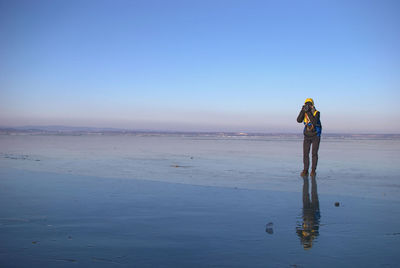 Man photographing in sea against clear sky