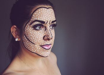 Close-up of young woman with face paint while standing on gray background