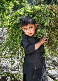 Portrait of boy carrying plant on shoulder outdoors