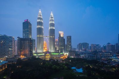 Illuminated petronas towers in city against clear blue sky at dusk
