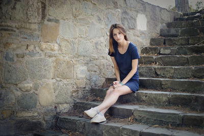 Young woman sitting on staircase against wall