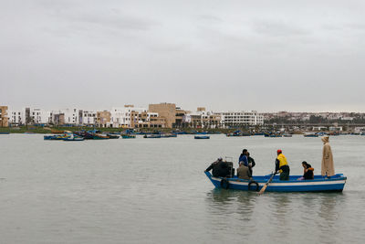 People on boat in river against sky in city